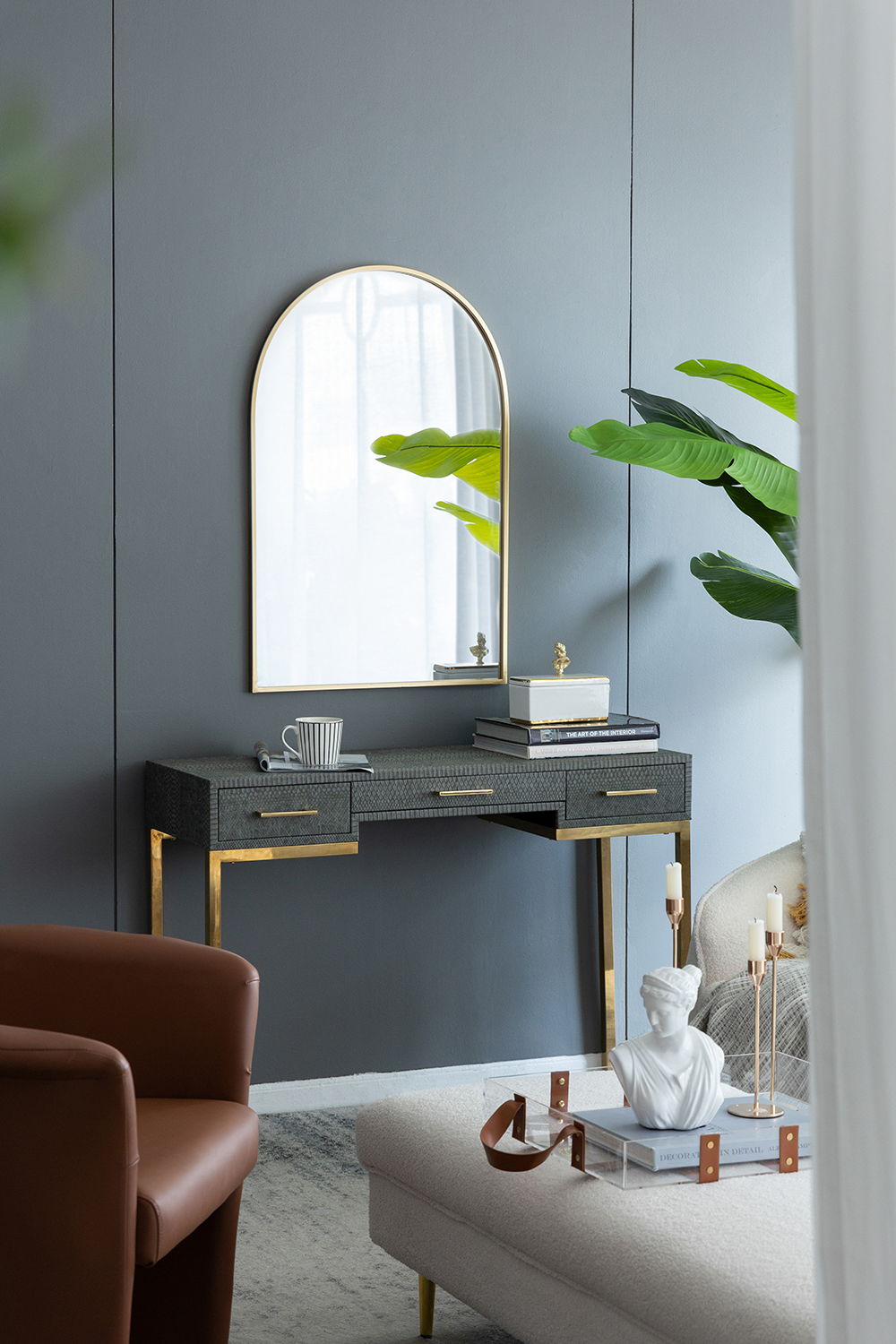Arched wall mirror with gold metal frame above a textured black console with gold legs on Tampa Home & Garden Store