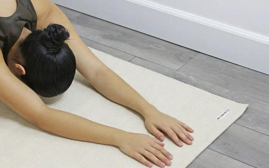 Yogi Organic Cotton Yoga Mat 78x27 in natural cream on wooden floor with user stretching on Tampa Home & Garden Store