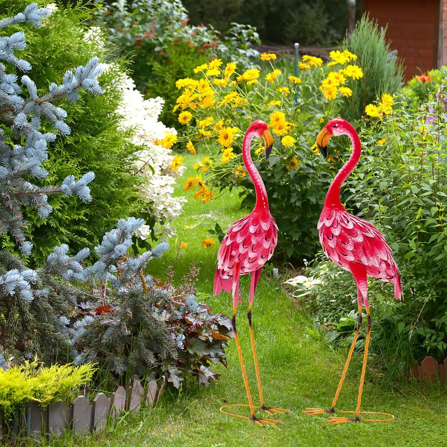 Two-piece pink flamingo garden statue set with long metal legs amid bright yellow flowers on Tampa Home & Garden Store