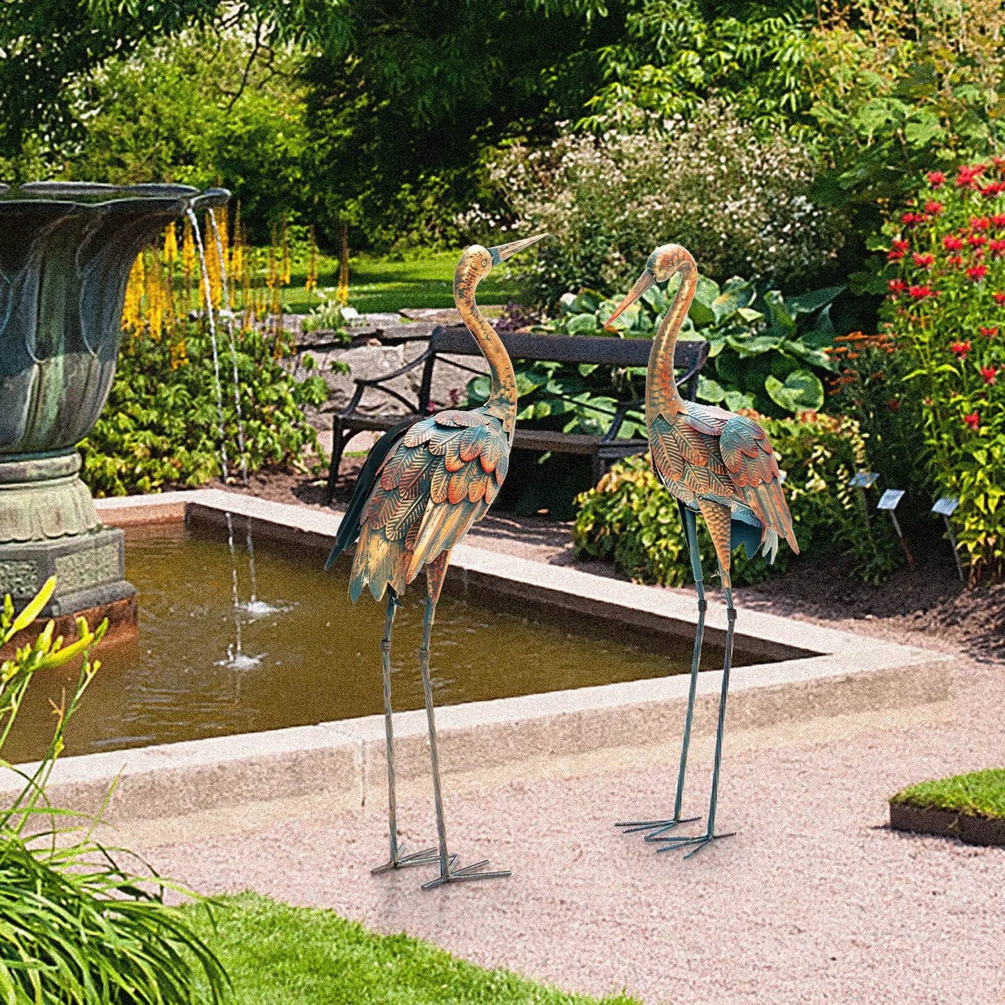 Set of 2 standing metal crane garden statues with patina finish on stake bases by a fountain on Tampa Home & Garden Store
