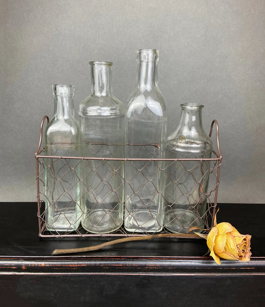 Four vintage glass apothecary bottles in a copper wire basket against a gray background on Tampa Home & Garden Store