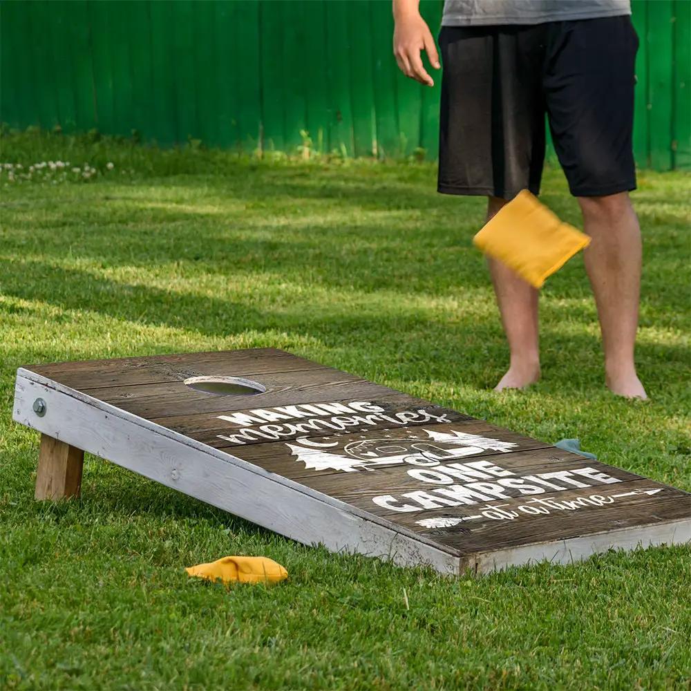 Cornhole board wrap Making Memories at Camp on wood grain surface with white lettering and a yellow bean bag nearby on Tampa Home & Garden Store
