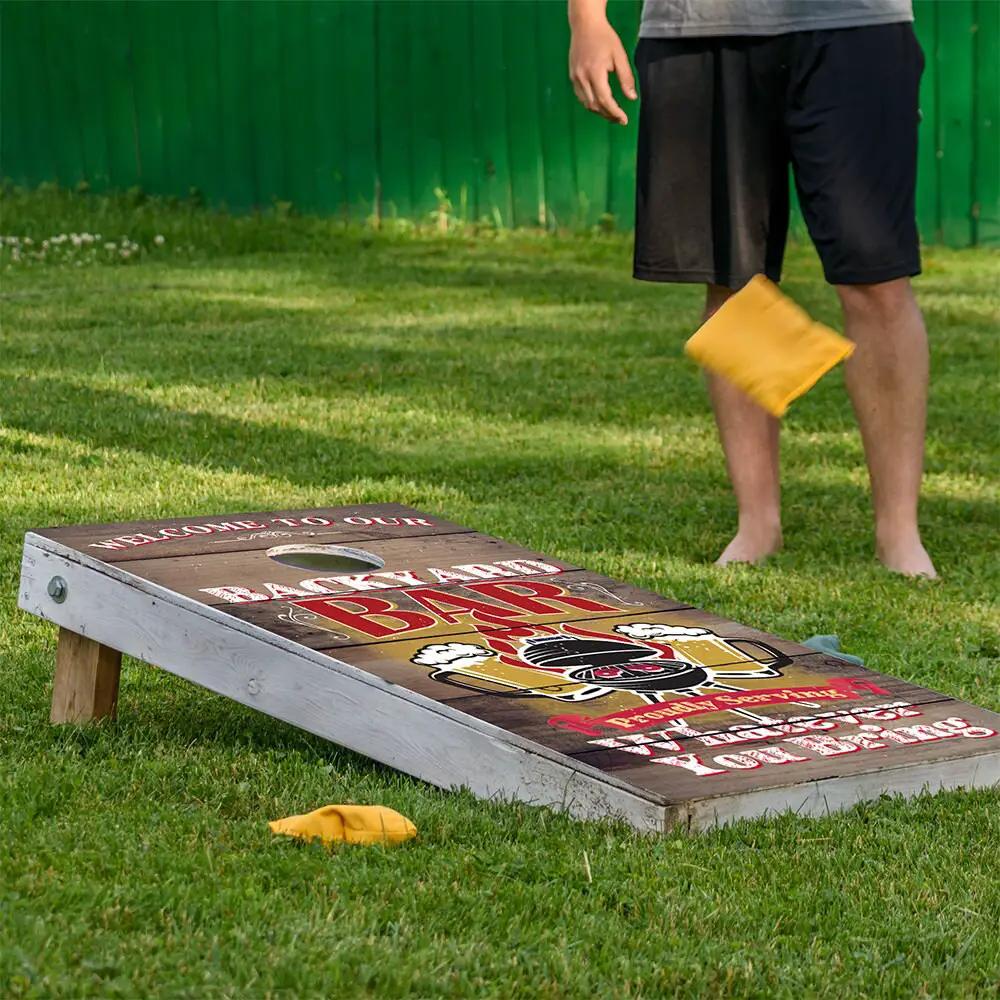 Backyard Bar Cornhole Board Wrap with wood-grain finish and bold red text on lawn yellow bags nearby on Tampa Home & Garden Store