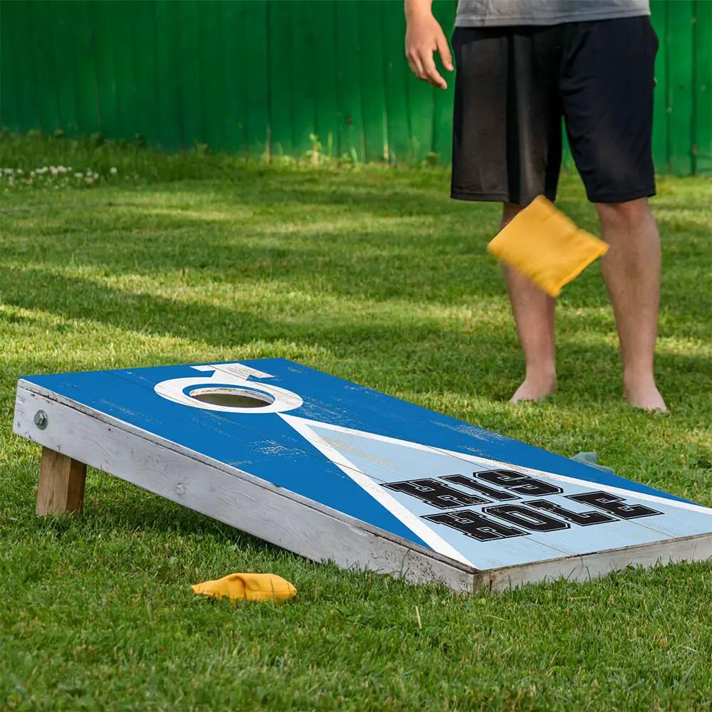 Cornhole board wrap set of 2 in blue with a white diagonal stripe on grass as a player tosses a yellow bean bag on Tampa Home & Garden Store