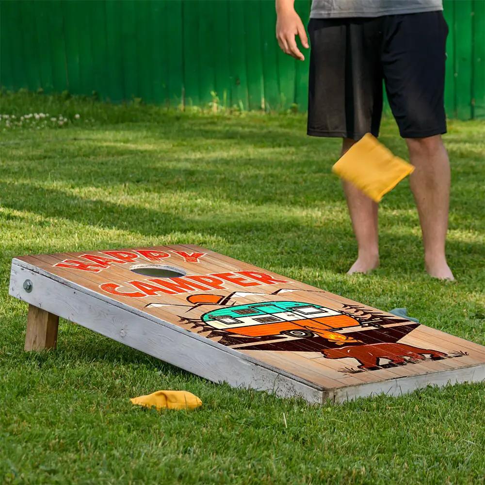 Happy Camper cornhole board wrap on wood with teal camper graphic and red text yellow bag nearby on Tampa Home & Garden Store