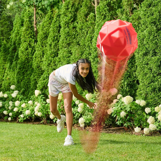 Aerobie Sonic Bounce ball red geometric orb in midair during outdoor garden play with a girl on Tampa Home & Garden Store