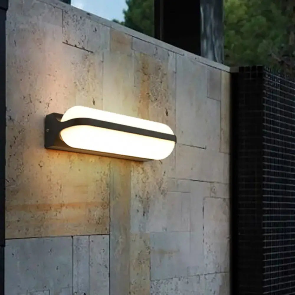 Black capsule flush mount wall sconce with white glass shade mounted on stone wall on Tampa Home & Garden Store