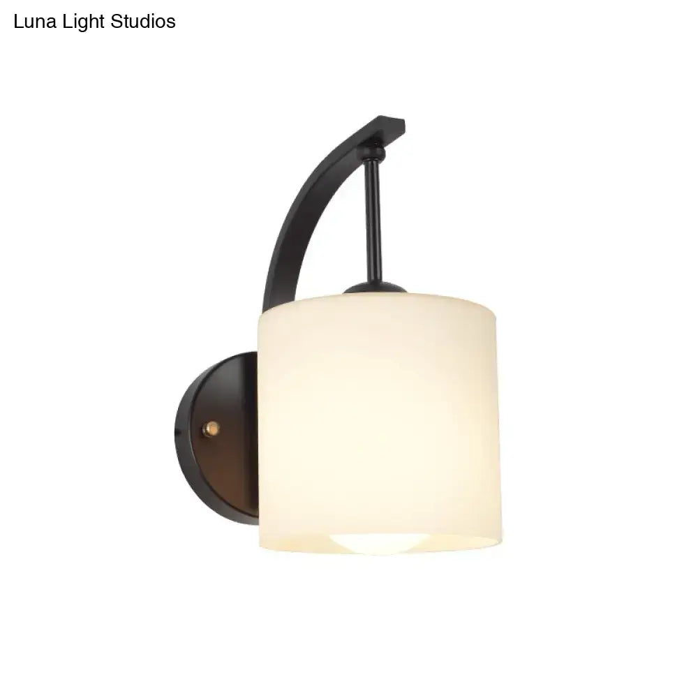 Black cylindrical opal glass sconce with a curved black metal arm and round backplate on Tampa Home & Garden Store