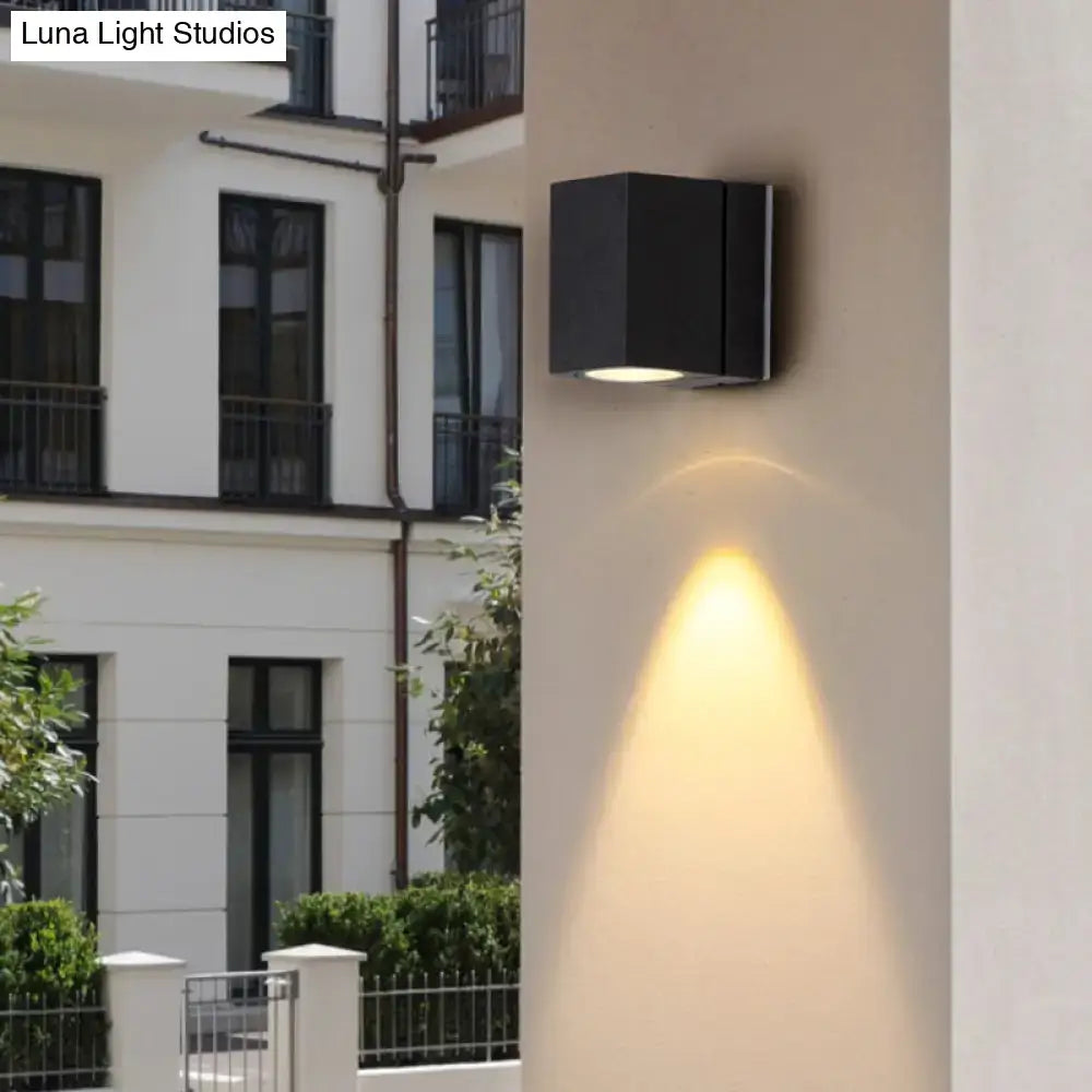 Black metal square mini wall sconce mounted on beige exterior wall, warm downward light on Tampa Home & Garden Store