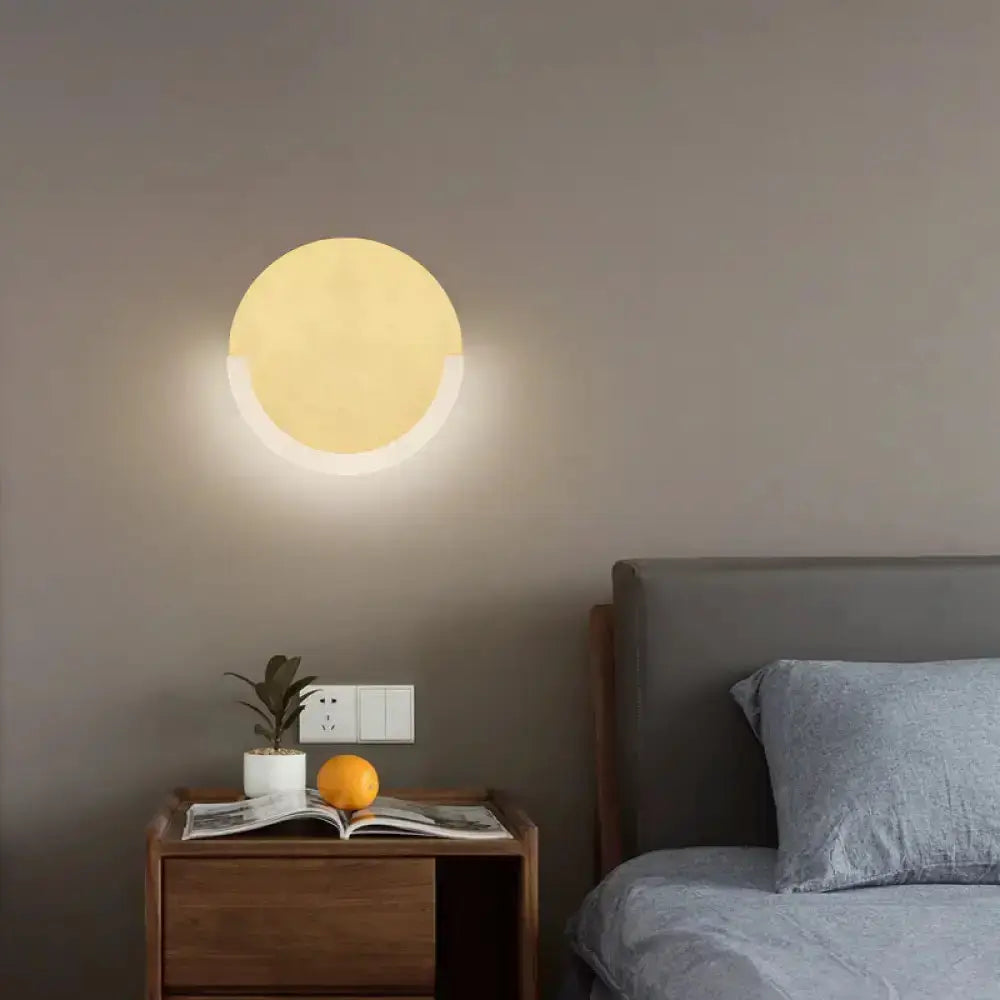 White and gold round acrylic LED wall sconce mounted above nightstand with warm glow on Tampa Home & Garden Store