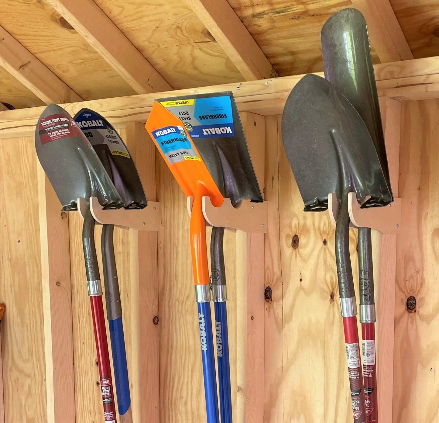 Tool rack for yard tools with colorful red blue and orange handles on wooden shed wall on Tampa Home & Garden Store