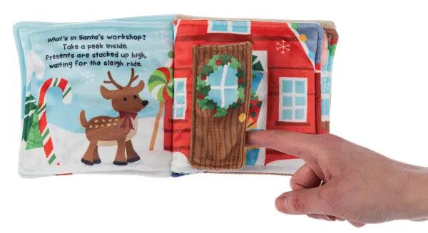 Baby soft fabric book Santa's Workshop with reindeer and door wreath scene; hand turning page on Tampa Home & Garden Store
