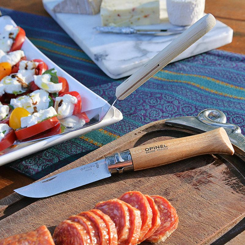Opinel folding knife with wooden handle and carbon steel blade on a cutting board beside sliced salami on Tampa Home & Garden Store