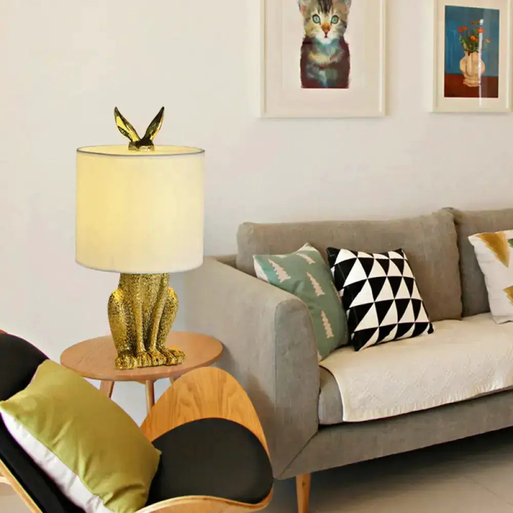 Gold glitter rabbit nightstand lamp with white drum shade on round wooden table beside gray sofa on Tampa Home & Garden Store