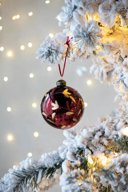 Glass Christmas ball ornament burgundy with gold leaf pattern hanging from snowy pine branch on Tampa Home & Garden Store