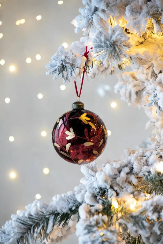 Glass Christmas ball ornament burgundy with gold leaf pattern hanging from snowy pine branch on Tampa Home & Garden Store