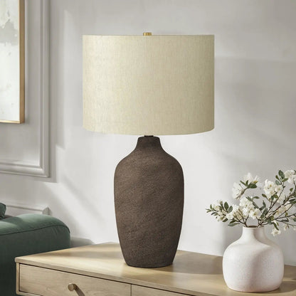 Table lamp with a dark textured ceramic base and beige fabric shade on a light wood table on Tampa Home & Garden Store