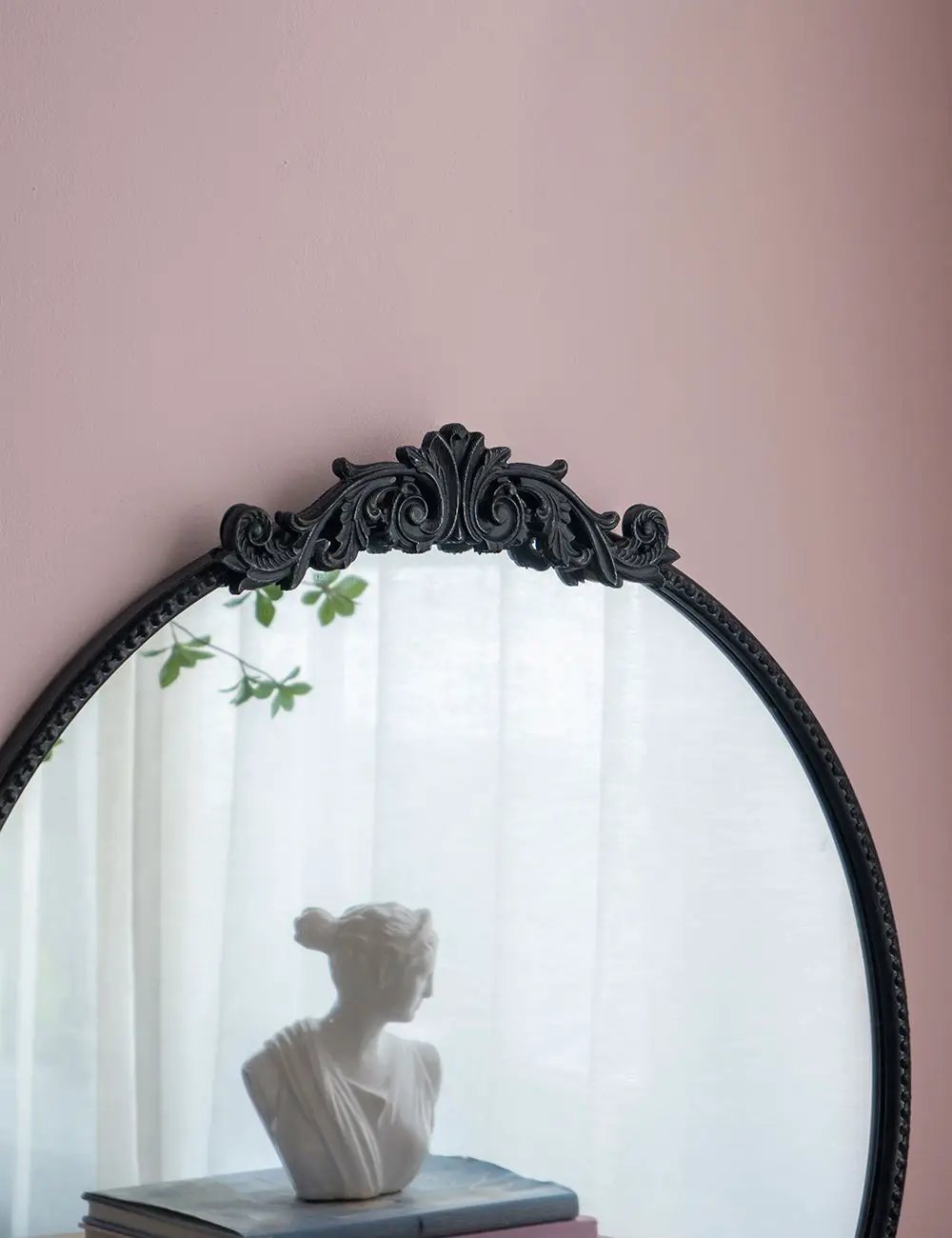 Round wall mirror with a black Baroque frame; ornate crest at top; reflects a bust on books on Tampa Home & Garden Store