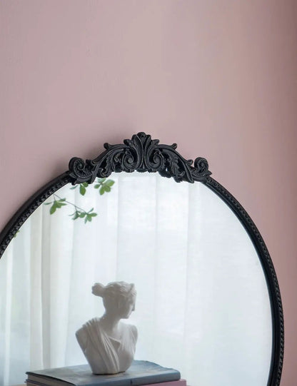 Round wall mirror with a black Baroque frame; ornate crest at top; reflects a bust on books on Tampa Home & Garden Store