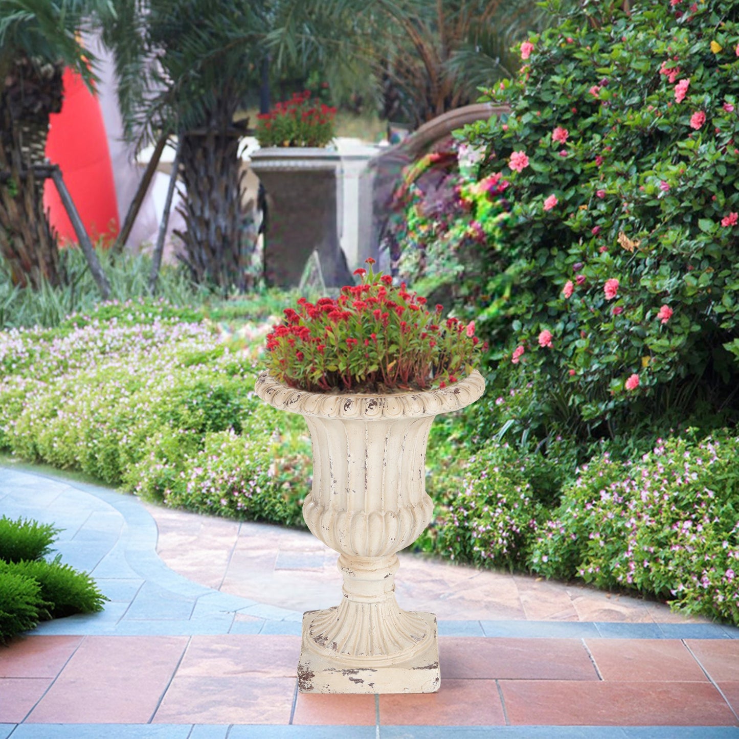 MGO Garden Urn antique white planter with red flowers on a decorative pedestal in a garden on Tampa Home & Garden Store