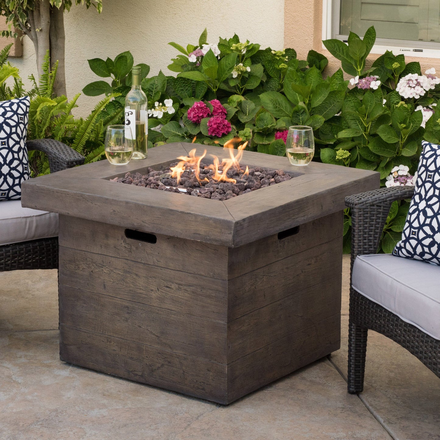 Anchorage 32'' Wood Square MGO Fire Pit Brown 40,000 BTU with wine bottle and two glasses nearby on Tampa Home & Garden Store