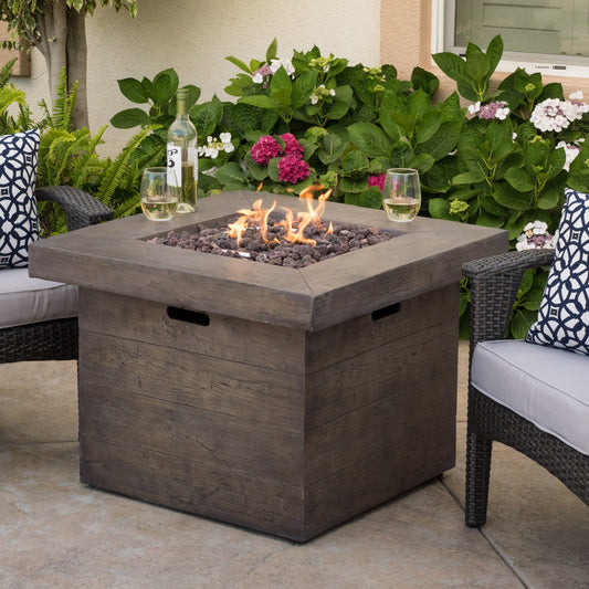 Anchorage 32'' Wood Square MGO Fire Pit Brown 40,000 BTU with wine bottle and two glasses nearby on Tampa Home & Garden Store