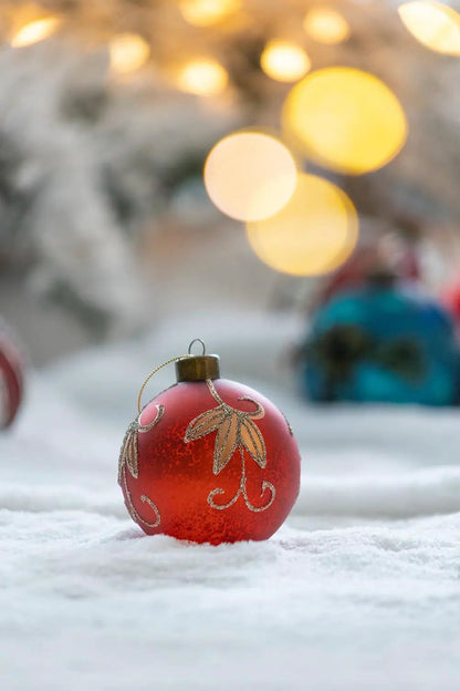 Red Christmas ball ornament with gold glitter pattern on snow, warm bokeh lights in background on Tampa Home & Garden Store