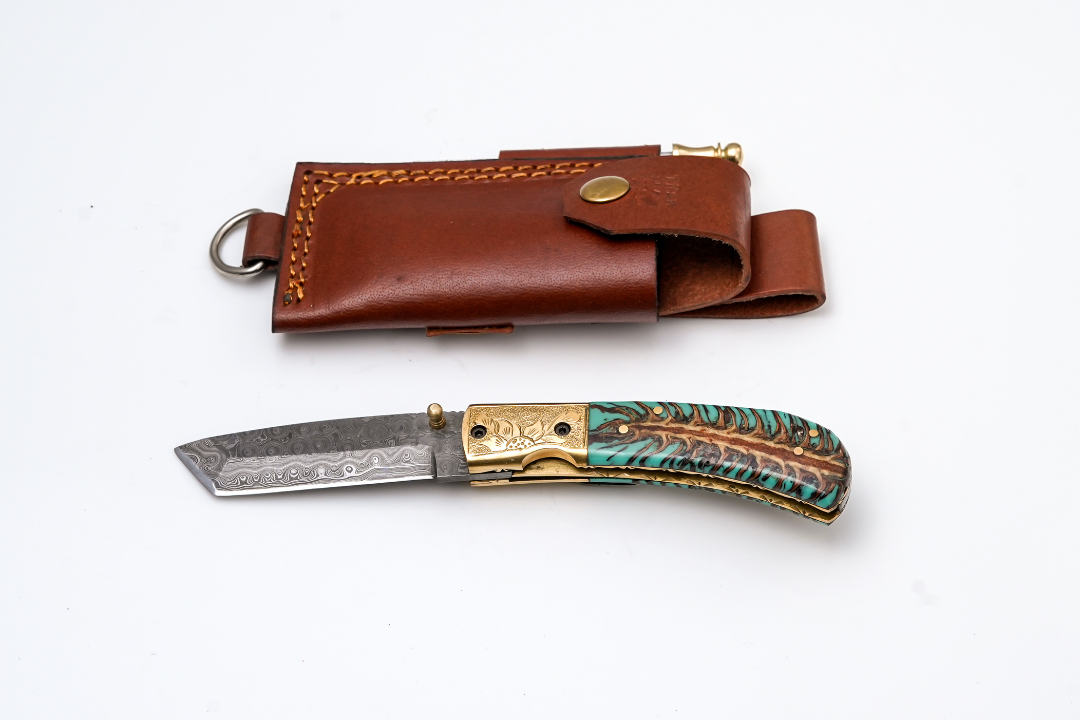 Damascus Tanto Folder from Titan K with teal pine cone handle and brass bolster in leather sheath on Tampa Home & Garden Store