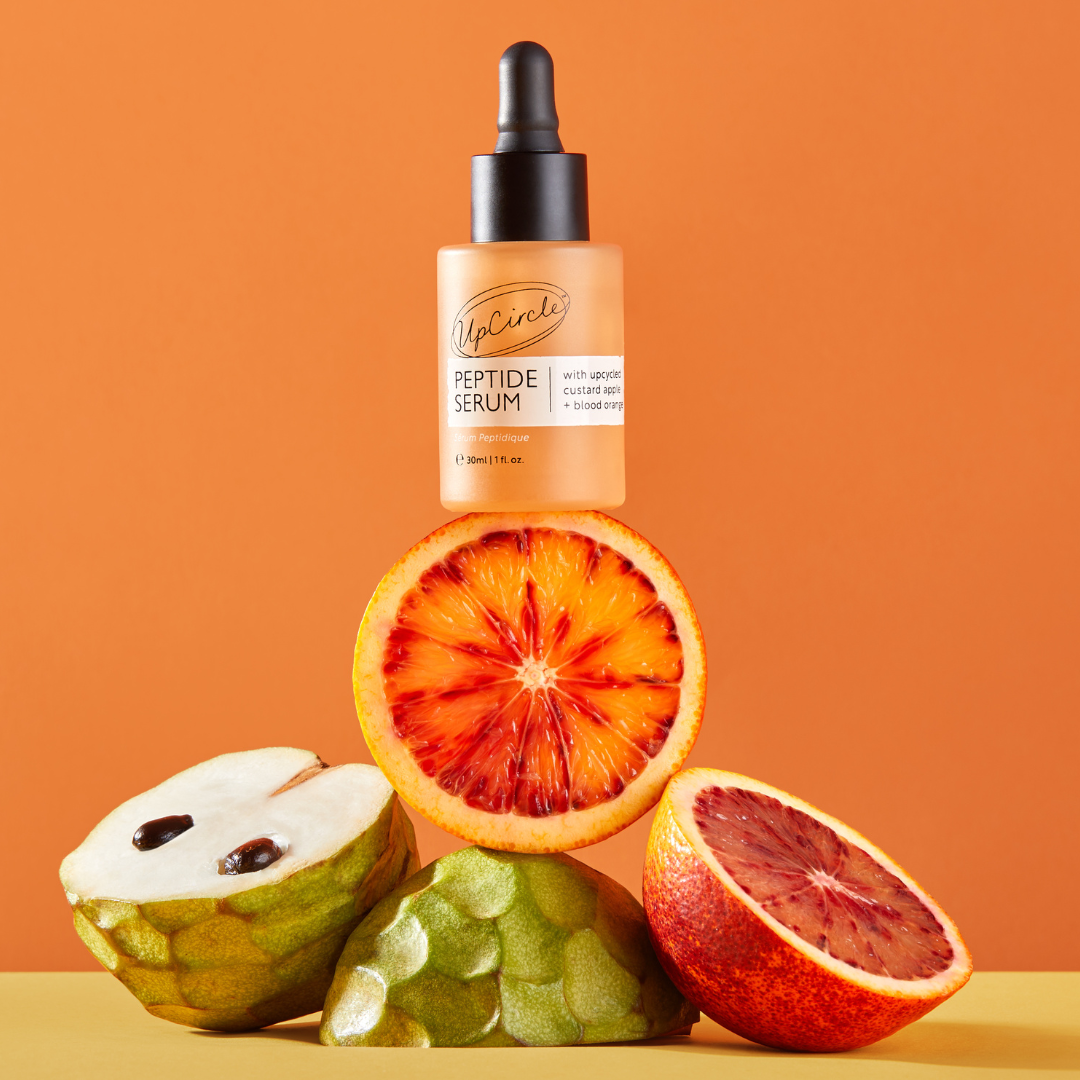 UpCircle Elasticity Boosting Duo peptide serum bottle with orange tint atop halved citrus on Tampa Home & Garden Store