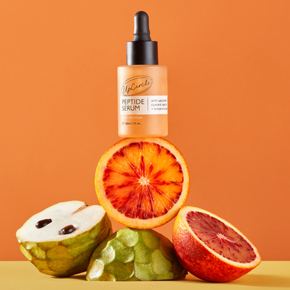 UpCircle Peptide Serum orange bottle with custard apple + blood orange atop citrus fruits on Tampa Home & Garden Store