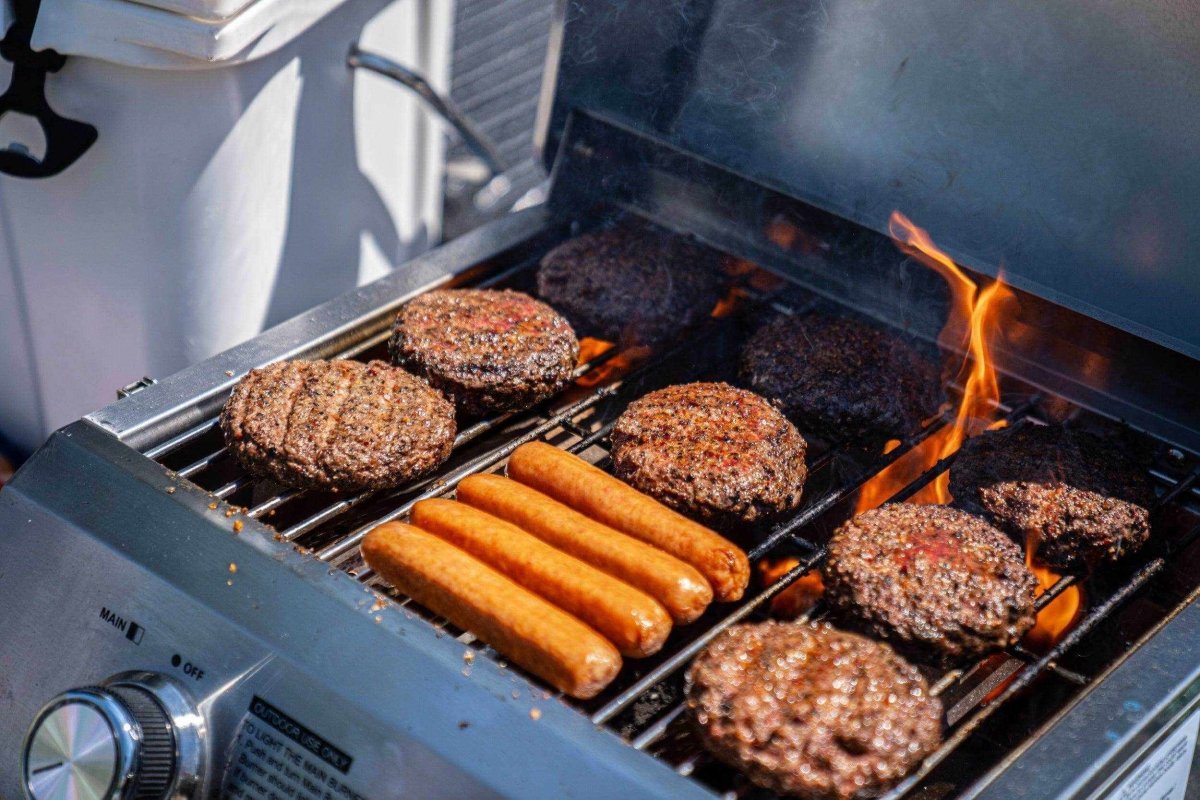 Stainless Tabletop Propane Grill by Monument Grills with burgers and sausages on the grate on Tampa Home & Garden Store