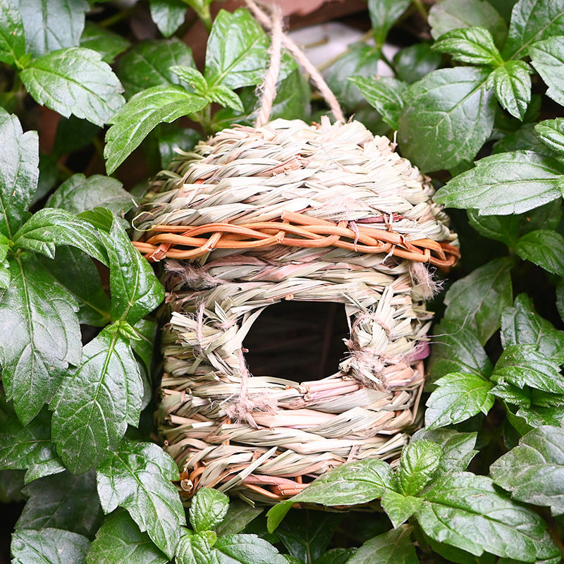 Handwoven straw bird nest cage with natural beige tones hanging among green leaves on Tampa Home & Garden Store