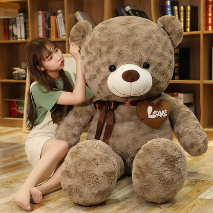Large brown teddy bear plush with white muzzle, brown nose, heart LOVE patch and brown ribbon on Tampa Home & Garden Store
