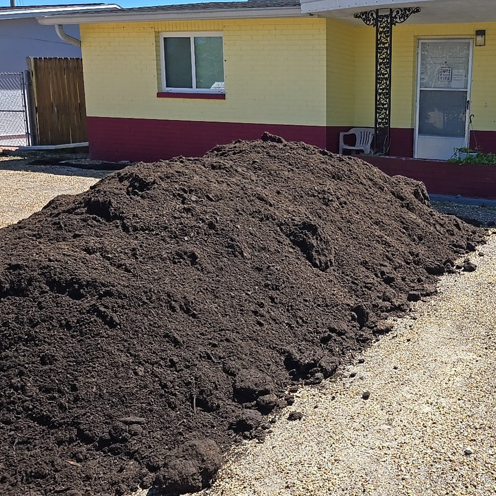 Pile of organic topsoil sold per cubic yard dumped in the front of a house that needs to grow grass.