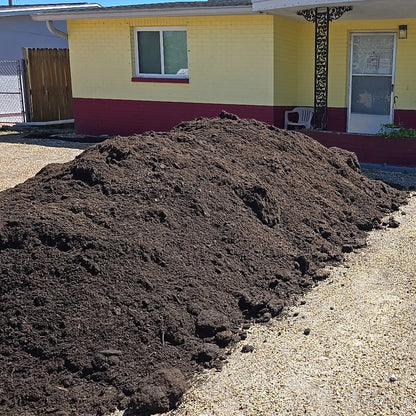 Pile of organic topsoil sold per cubic yard dumped in the front of a house that needs to grow grass.
