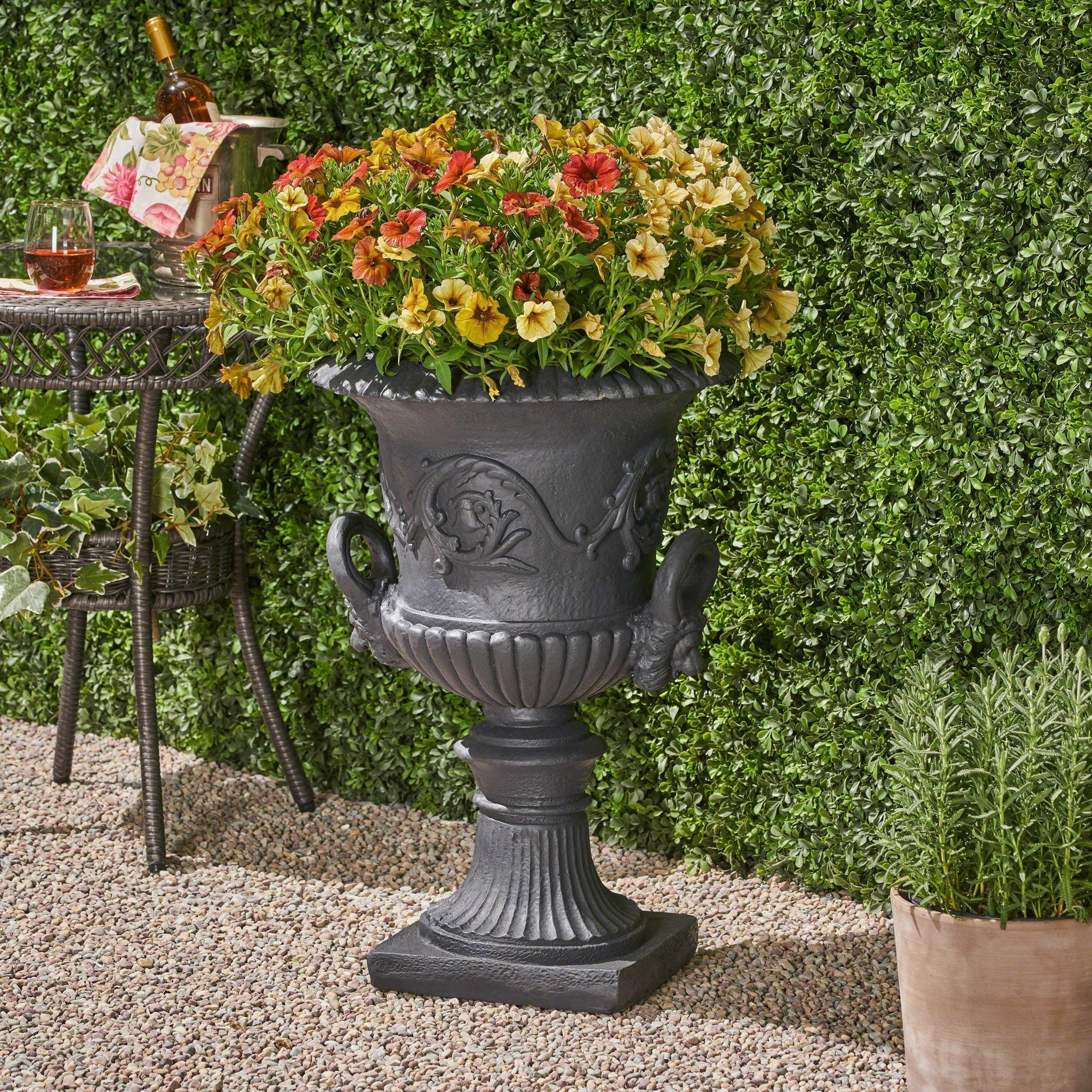 MGO Garden Urn Planter in dark gray metal filled with orange, yellow, and red petunias on Tampa Home & Garden Store