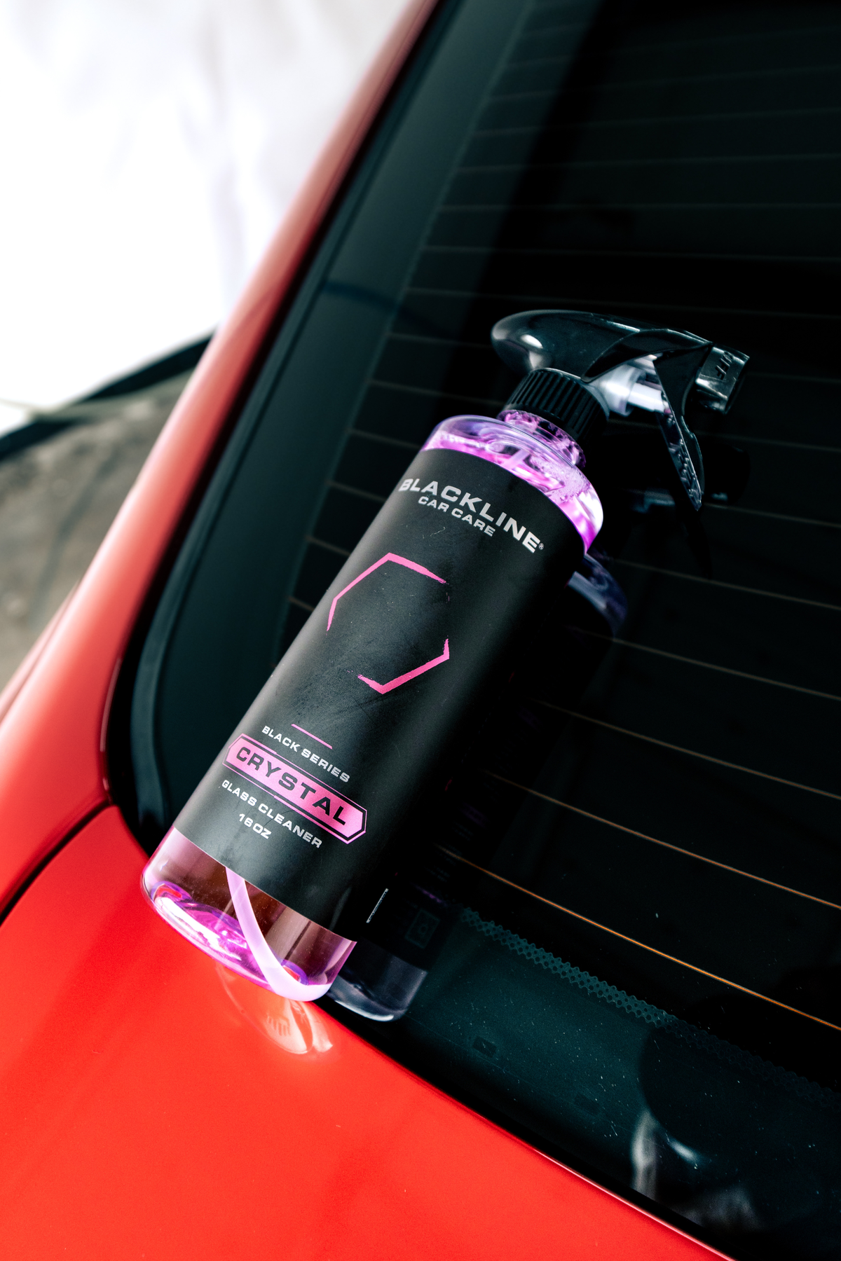 Crystal Glass Cleaner spray bottle by Blackline Car Care with purple liquid on a car window on Tampa Home & Garden Store