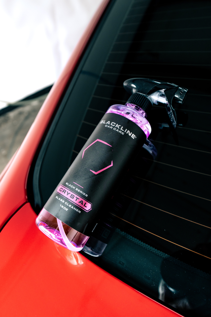 Crystal Glass Cleaner spray bottle by Blackline Car Care with purple liquid on a car window on Tampa Home & Garden Store