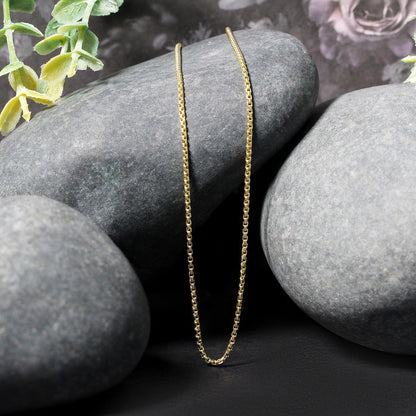 Two 14k yellow gold round box chain necklaces 1.35 mm draped over smooth gray stones on Tampa Home & Garden Store