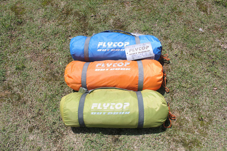Flytop outdoor camping tents rolled in blue, orange, and olive sacks with logo on grass on Tampa Home & Garden Store