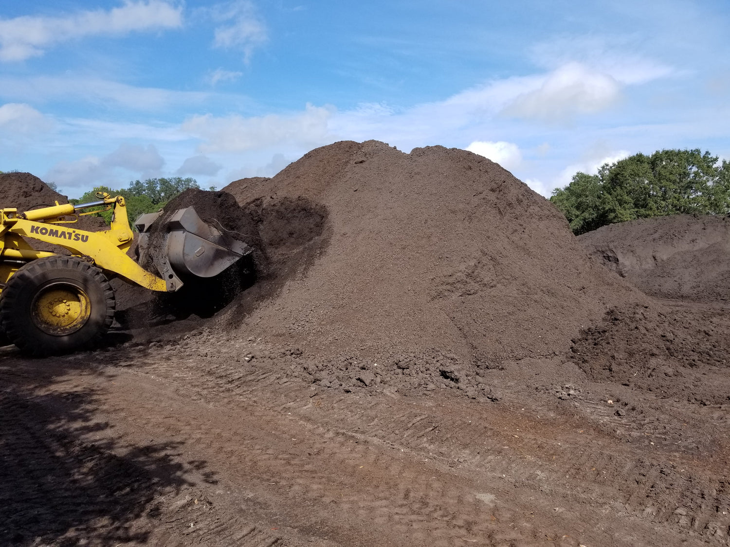 Buy piles of landscape materials and machine scooping up landscaping soil.