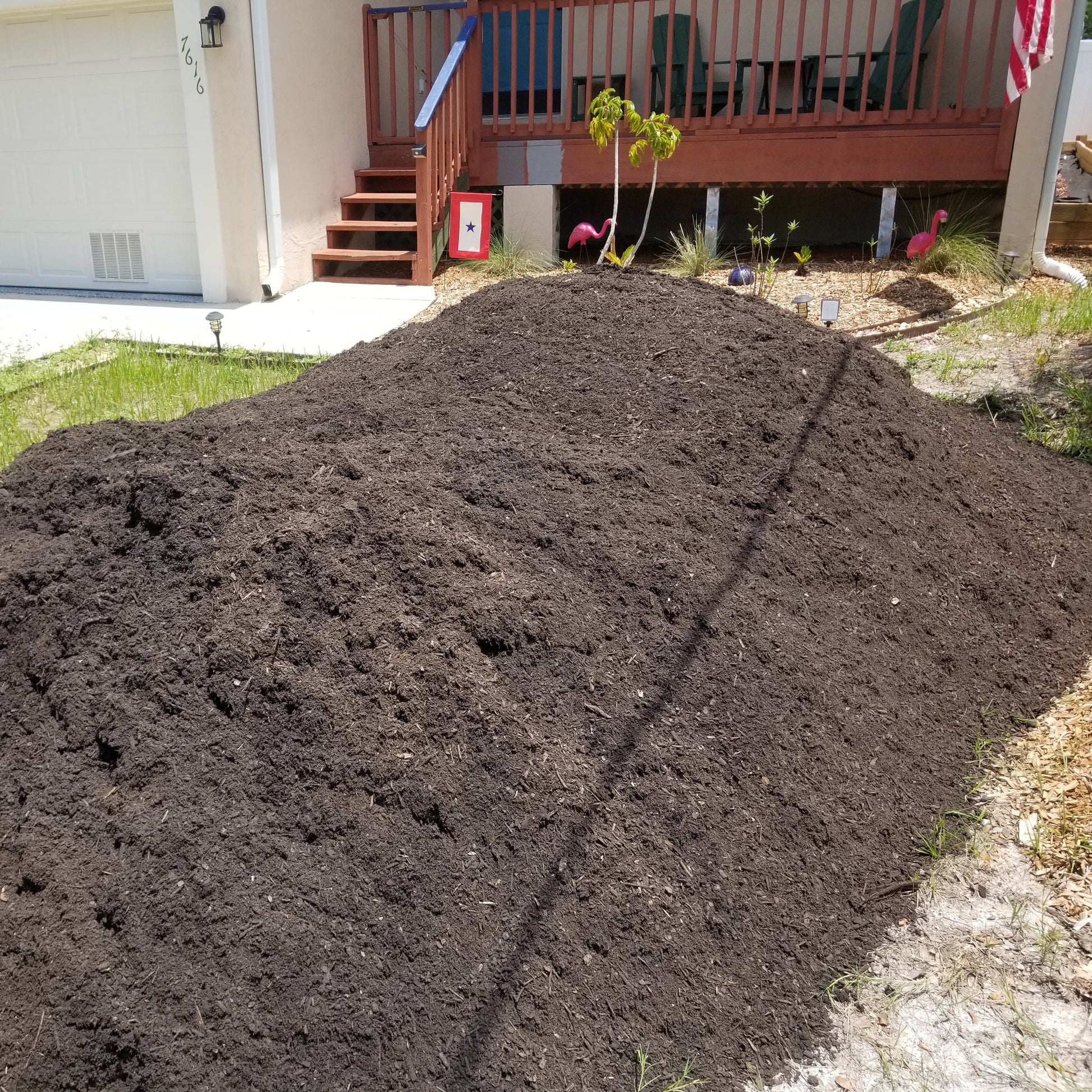 Large pile of dark brown garden soil delivered to the front yard at a residential home.