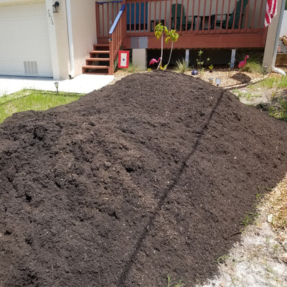 Large pile of dark brown garden soil delivered to the front yard at a residential home.