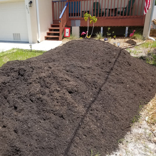 Large pile of dark brown garden soil delivered to the front yard at a residential home.