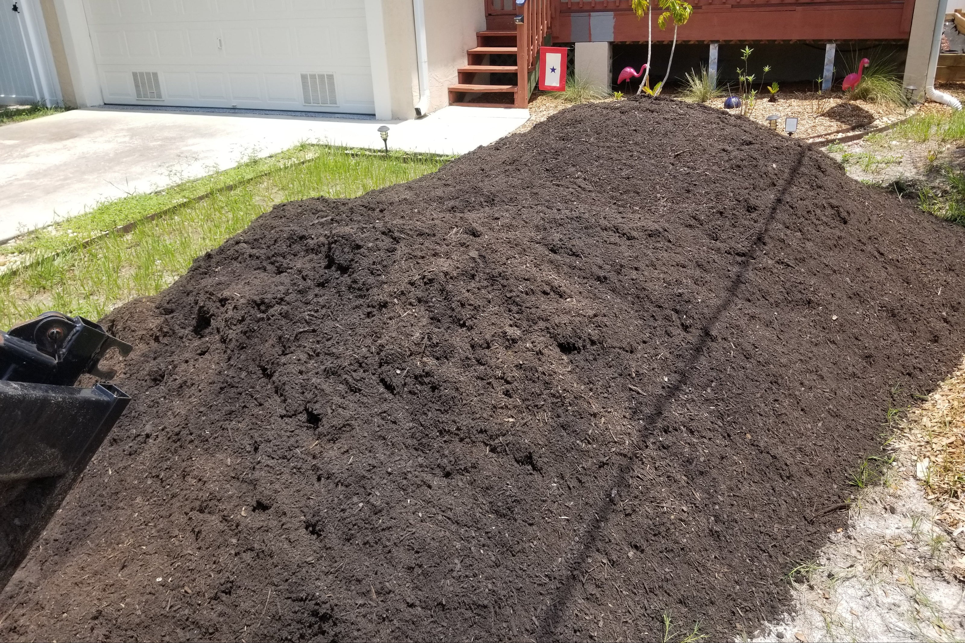Large pile of dark brown compost in a residential front yard.
