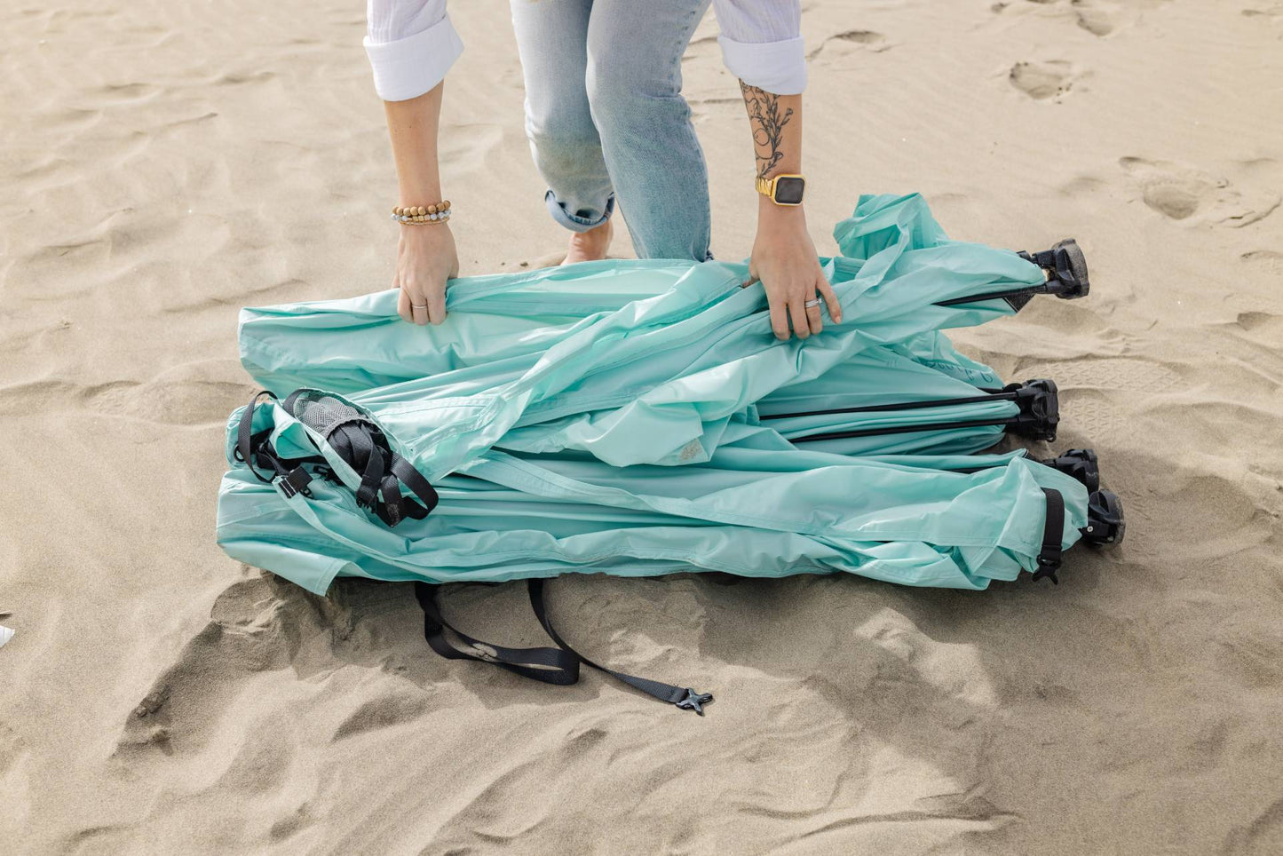Pop 'N Go canopy turquoise folded bundles with black straps on sandy beach on Tampa Home & Garden Store