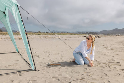 Pop 'N Go canopy mint-green with black poles on a sandy beach beside a kneeling woman on Tampa Home & Garden Store