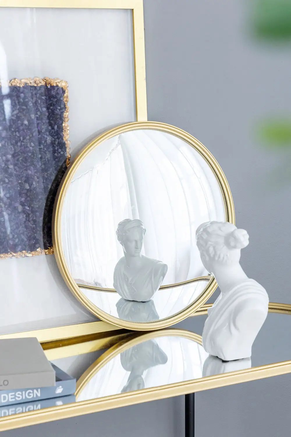 Round wall mirror with a gold iron frame reflecting white bust beside a textured art panel on Tampa Home & Garden Store