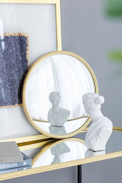 Round wall mirror with a gold iron frame reflecting white bust beside a textured art panel on Tampa Home & Garden Store