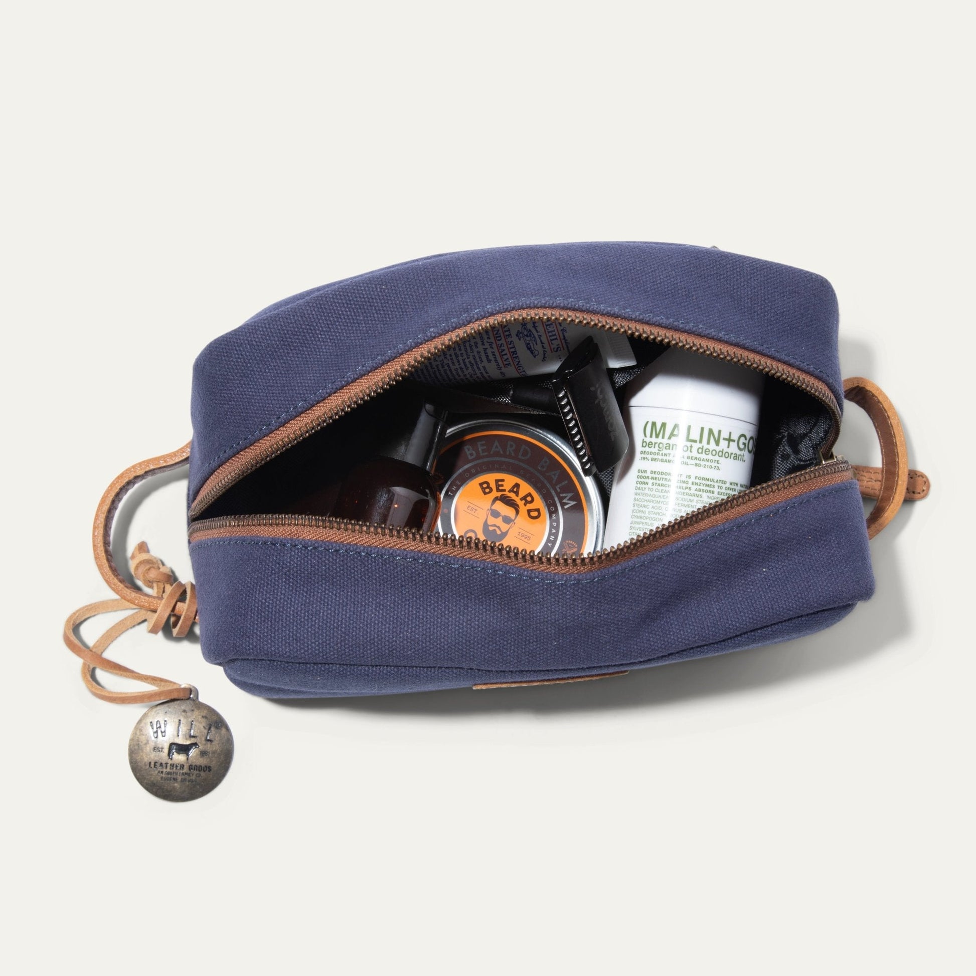 Commuter Travel Kit toiletry bag by Will Leather Goods, navy canvas with tan leather trim, opened to reveal grooming bottles and tins on Tampa Home & Garden Store